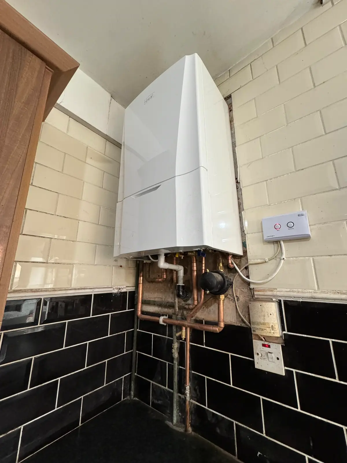 Combi boiler mounted in the corner of a tiled utility area with copper pipework dropping to floor level