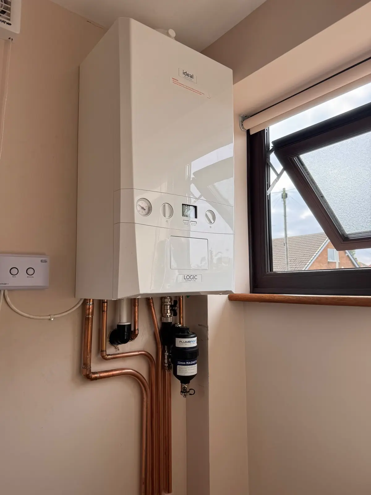 Ideal Logic combi boiler fitted beside a window, with copper pipework and a magnetic system filter below it