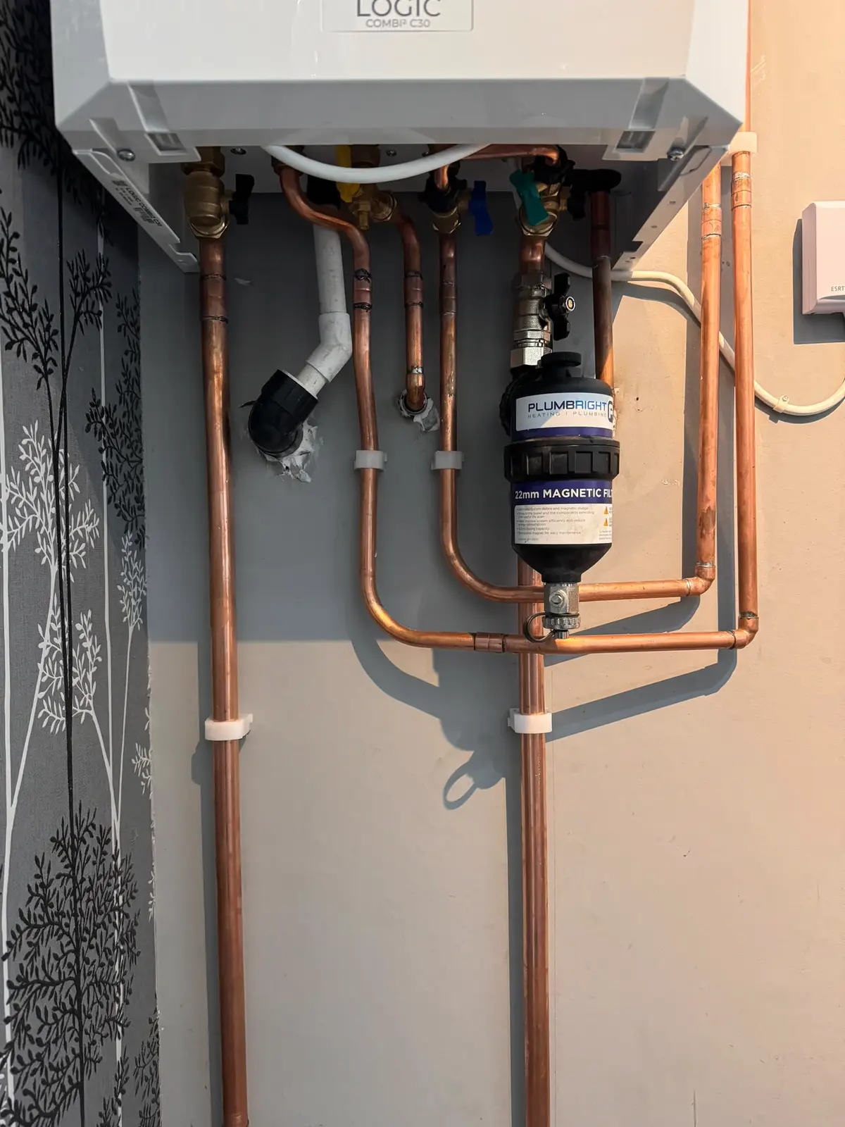 Close-up of copper pipework, isolation valves and a 22mm magnetic filter beneath a combi boiler