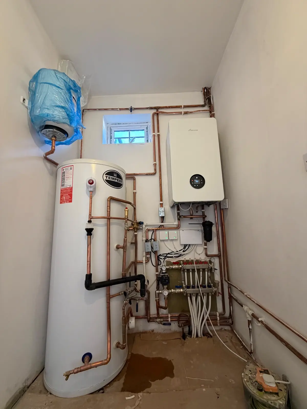 Unvented hot water cylinder piped in copper next to a wall-mounted boiler and a heating manifold