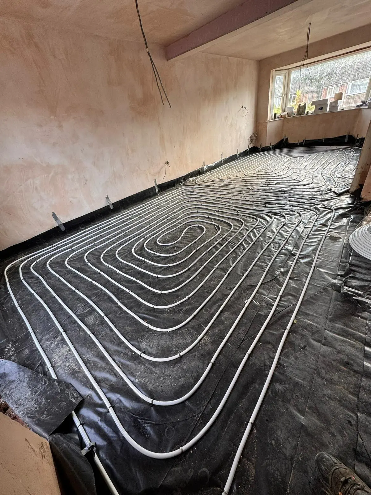 Underfloor heating pipe laid in a spiral pattern over a black membrane across a whole room before screeding